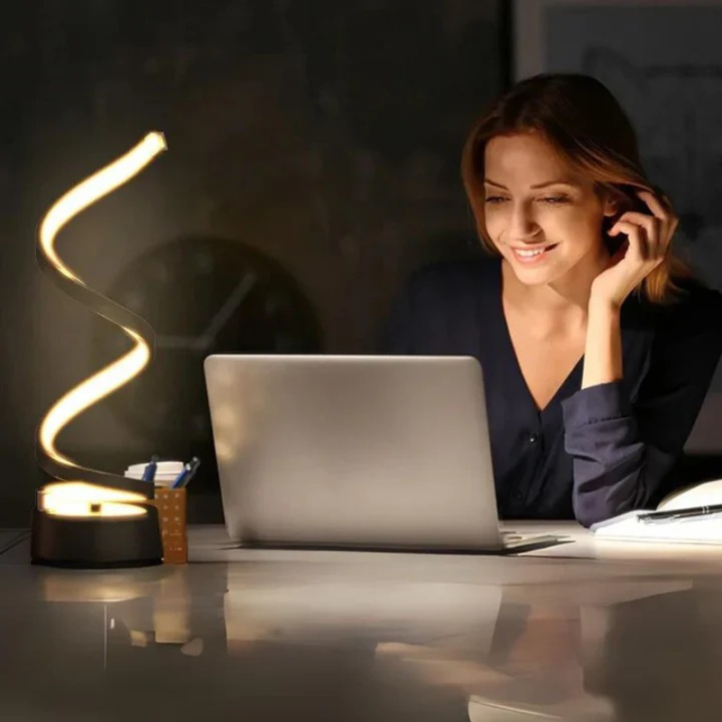 Moderne spiralförmige LED-Tischlampe, die auf einem hölzernen Beistelltisch in einem gemütlichen Interieur warm leuchtet